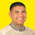 A Latino man smiles for the camera in a checked colored shirt with a bright yellow background.