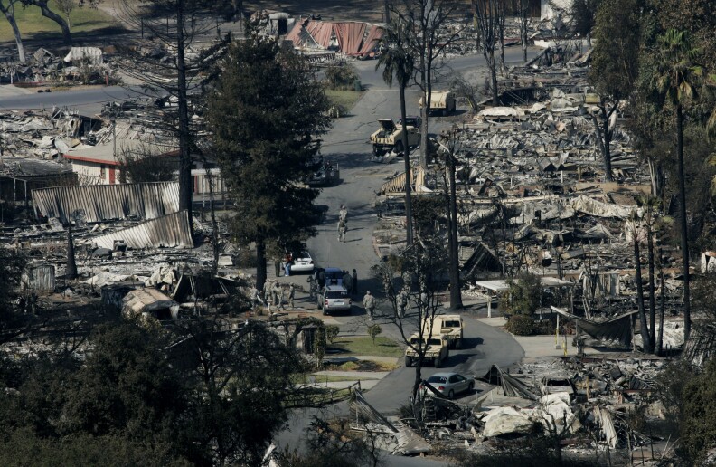 A burned down neighborhood with few people walking the streets.