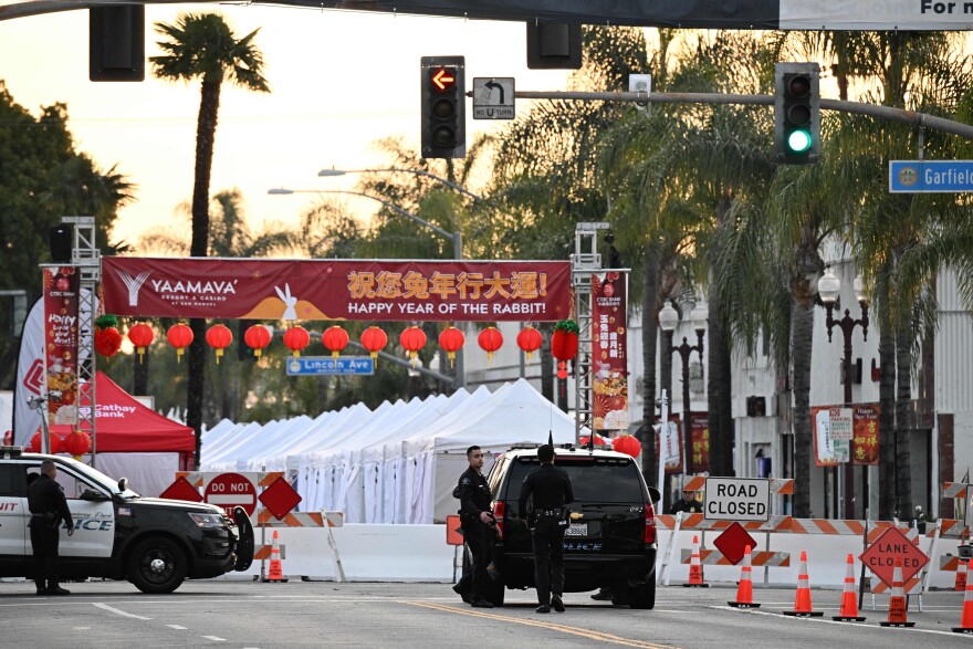 Police SUV's are parked in front of a barricade with "Road Closed" and "Do Not Enter" signs. A line of red and white tented stalls are set up on the other side and recede into the distance. A red banner stretches over the road overhead that has Chinese characters and in English, "Happy Year of the Rabbit," and includes what looks to be the name of a corporate sponsor, Yaamava' Resort and Casino at San Manuel.