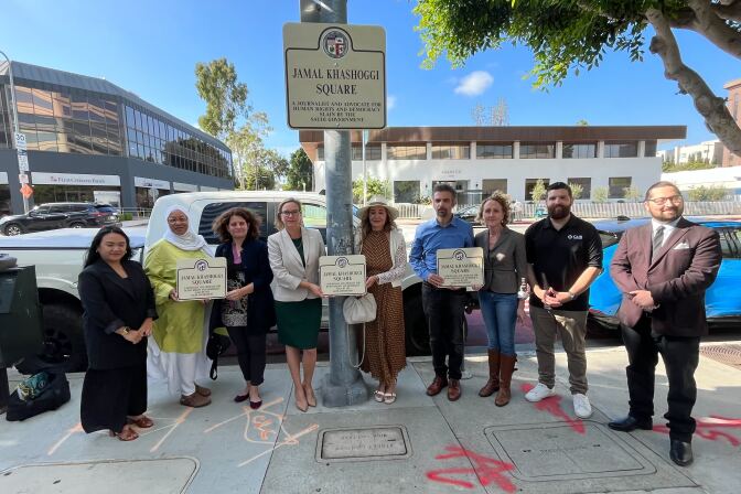 Nine people stand beside a street signed named Jamal Khashoggi Square. Cars and buildings are visible in the background.