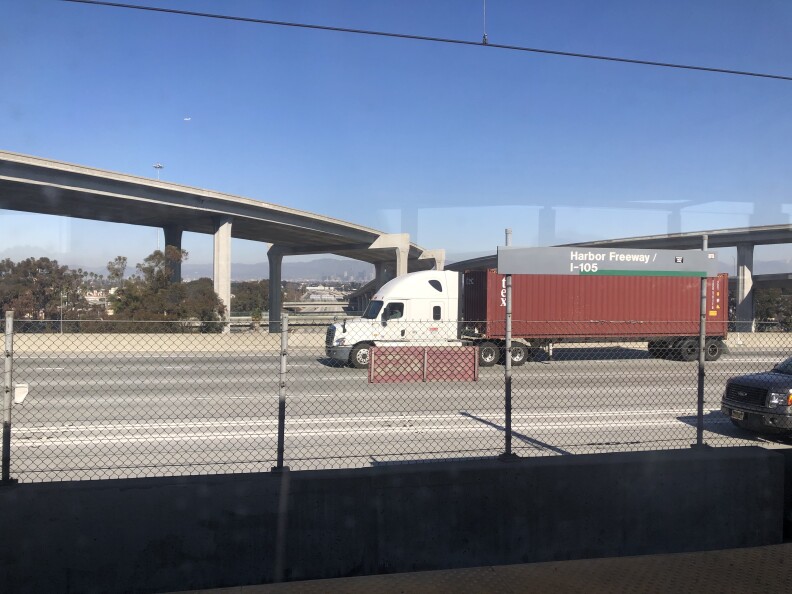 A red truck drives past on the freeway, as the downtown LA skyline appears in the distance