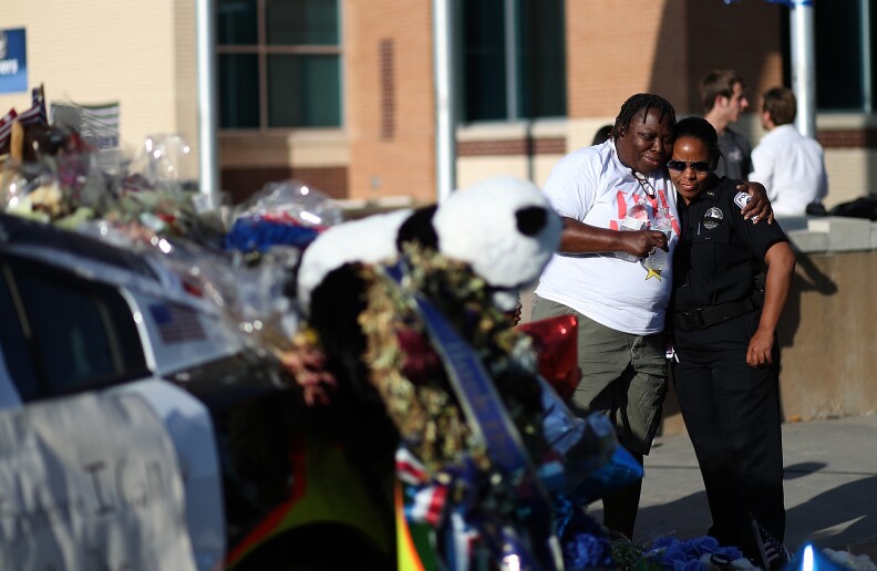 DALLAS, TX - JULY 13:  A mourner hugs a police officer in front of the Dallas Police department headquarters on July 13, 2016 in Dallas, Texas. Funerals have begun for 5 Dallas police officers who were shot and killed by a sniper during a Black Lives Matter march in Dallas.  (Photo by Justin Sullivan/Getty Images)
