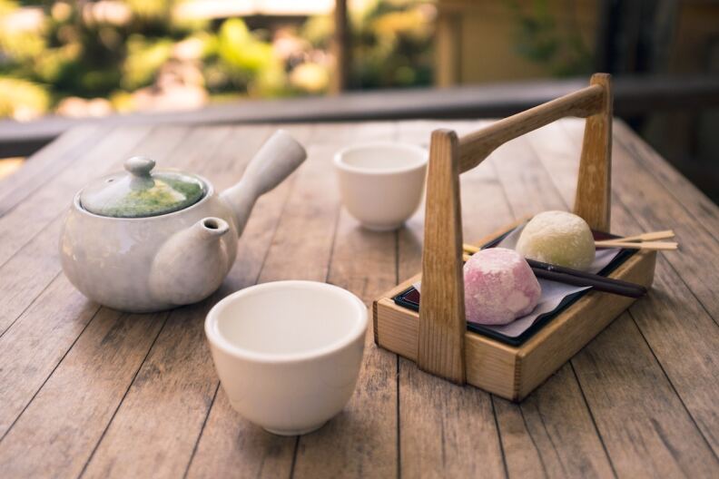A tea set-up in a Japanese tea garden in the daytime with a pot, cups and mochi on a wooden table.
