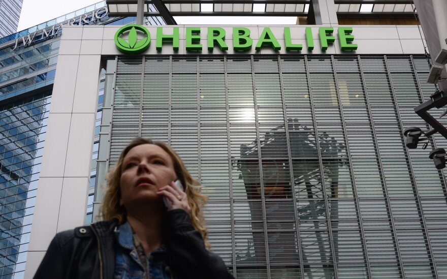 A woman is seen speaking on her cellphone beneath a Herbalife sign atop an office building in downtown Los Angeles on January 24, 2014. A US Senator is urging federal regulators to investigate the business practices of Herbalife Ltd., the Los Angeles maker of nutrition and personal care products. Massachusetts Democrat Edward J. Markey asked the Securities and Exchange Commission and Federal Trade Commission to investigate Herbalife, with concern coming some 13 months after hedge fund manager Bill Ackman accused Herbalife of operating a pyramid scheme. AFP PHOTO/Frederic J. BROWN (Photo credit should read FREDERIC J. BROWN/AFP/Getty Images)