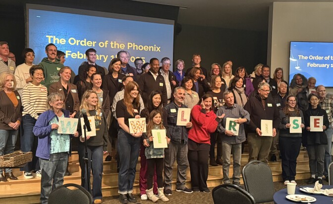 A group of about 50 people stand in front of a screen that says "The Order of the Phoenix." Many pictured lost their homes in the Eaton Fire. 