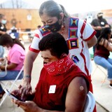 LOS ANGELES, CALIFORNIA - APRIL 10: Volunteer Miriam Lopez Ambrosio (TOP), a folkloric dancer from Oaxaca, assists a person with their second vaccination appointment on their phone at a clinic targeting Central American Indigenous residents at CIELO, an Indigenous rights organization, on April 10, 2021 in Los Angeles, California. CIELO launched an outreach campaign for vaccinations to address language barriers, accessibility, mistrust of government and misinformation among Mexican and Guatemalan Indigenous residents. They have suffered disproportionately during the pandemic with many losing work in the hospitality industry. St. John's Well Child and Family Center is administering COVID-19 vaccines across South L.A. in a broad effort to bring vaccines to minority communities. (Photo by Mario Tama/Getty Images)