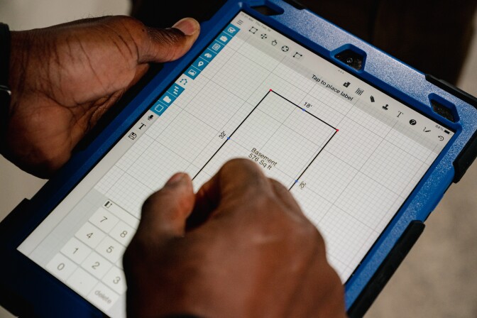 A person with dark-tone skin uses a tablet to mark measurements