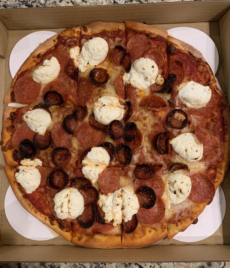 A pizza pie is placed in a pizza box, with white protective paper placed beneath it. 