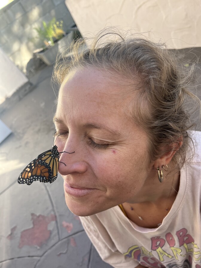 A woman smiles with a monarch butterfly on her nose.
