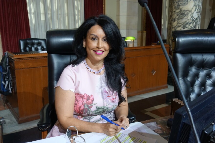 Nury Martinez, a light brown woman with dark hair, is wearing a pink dress and is seated behind a desk.