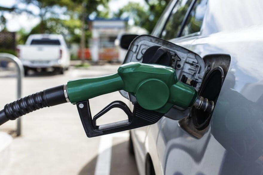 A green gas pump, pumping gas into a silver car.