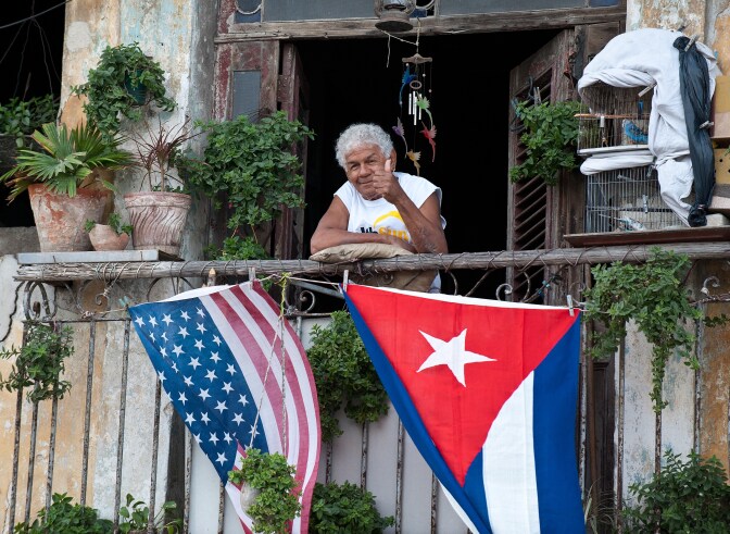 A Cuban gives the thumbs up from his balcony decorated with the US and Cuban flags in Havana, on January 16, 2015. The United States will ease travel and trade restrictions with Cuba on Friday, marking the first concrete steps towards restoring normal ties with the Cold War-era foe since announcing a historic rapprochement.