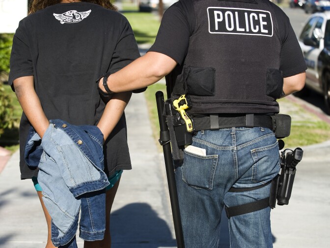 After arresting Toya Latrice Daniels,  Buena Park police officer James Woo, left, walks Daniels in his patrol car for transportation to the Buena Park Police Department. Daniels was charged with one misdemeanor count of contributing to the delinquency of a minor and one misdemeanor count of failure to reasonably supervise or encourage school attendance. By March of the school year, her elementary school child had accumulated 17 unexcused absences.