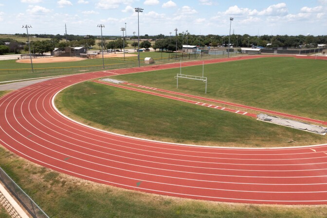 A red track and field track has eight lanes, a shotput pit and a grassy field.