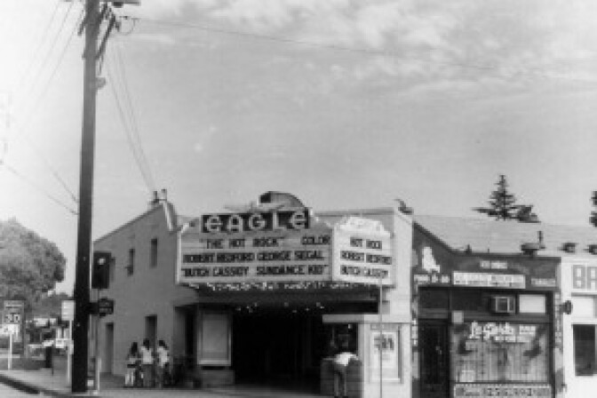 Black and white photo of the front of a street corner theatre with a marquee covered in letters and the word Eagle above it. 