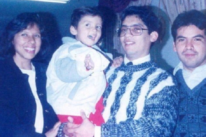 A slightly faded photo of a Latino man with glasses, smiling. holding a little boy with a jacket, red pants and brown hair. He is flanked by a smiling Latina with a bob haircut and a black jacket, and another man with dark hair and a faint mustache. 