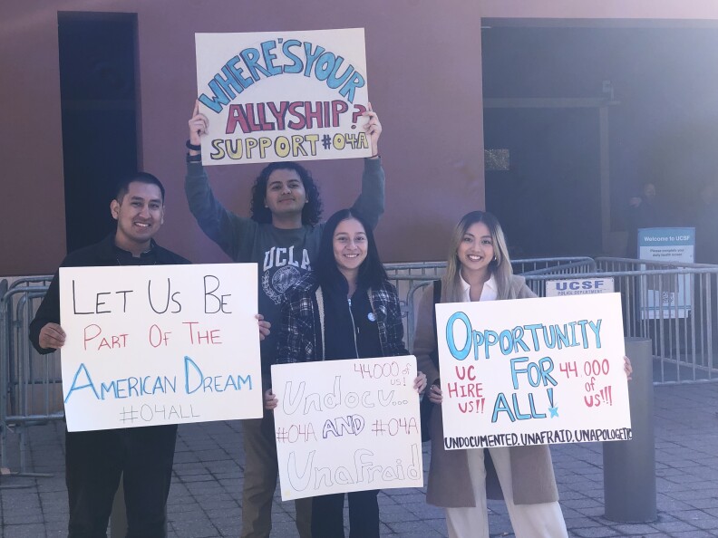 Four young adults with light brown skin hold hand-lettered signs