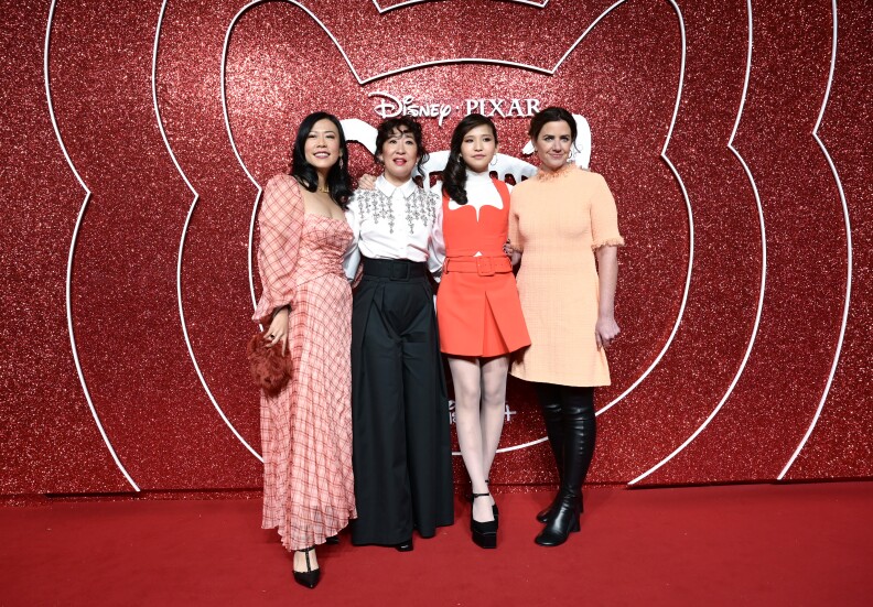 Four actors from Turning Red pose arm-in-arm in front of a red sparkly backdrop.