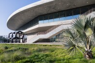 A building made of concrete and glass. Grass and palm trees are in front of the building.