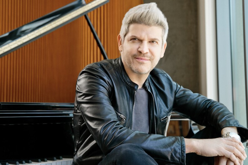 a man in a black leather jacket sits at a piano