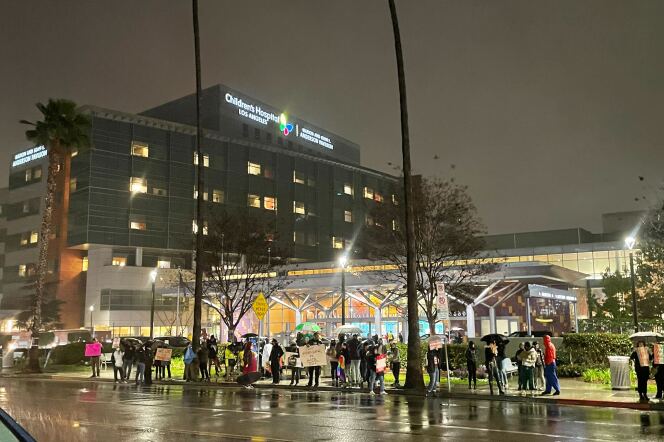 Dozens of protesters holding signs on a rainy night outside of a hospital.