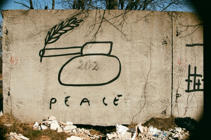 A cement wall with a military tank and the word "peace" painted on it