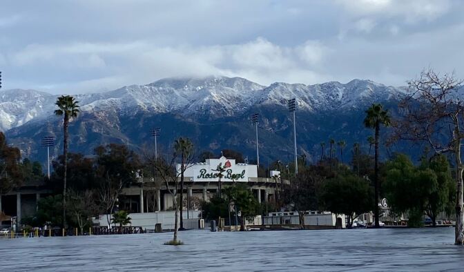 Snow capped mountains rise above the Rose Bowl stadium with palm trees in the foreground