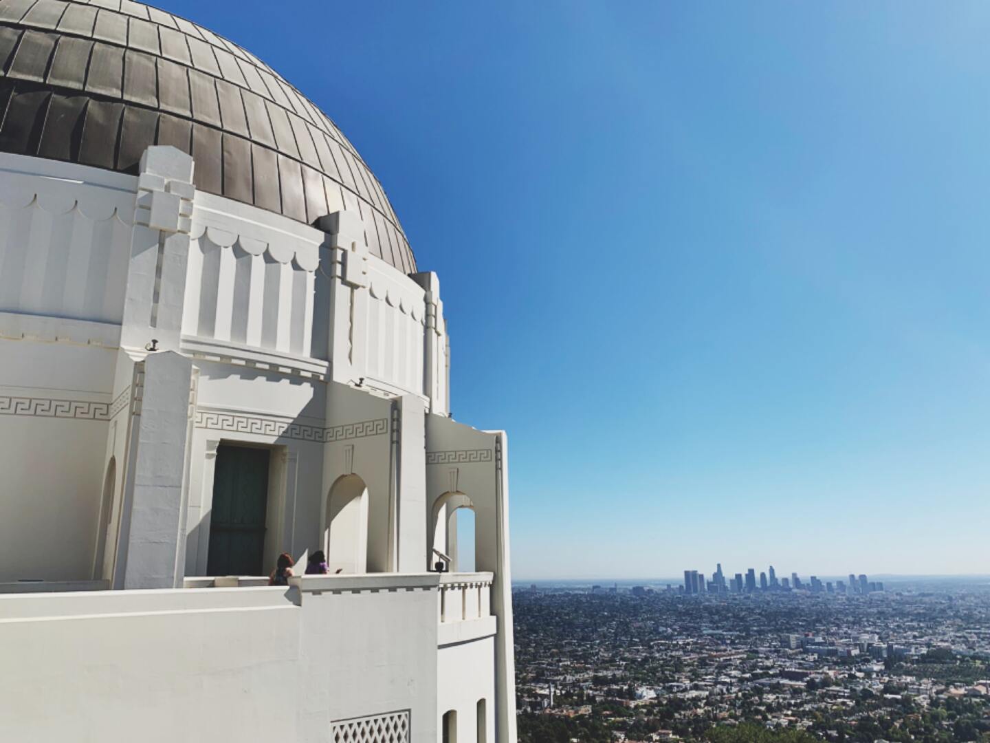 the white observatory with its black dome look over Los Angeles on a sunny day. downtown is visible in the distant background