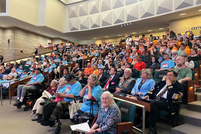 Rows and rows of seats are filled with residents, many wearing sky blue shirts that read "Build It Now" referring to a veterans cemetery. Others, wearing orange, want to stick to plans to build the cemetery in Anaheim.