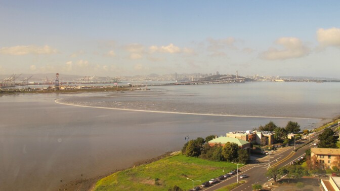 A low level wave heads to shore near a port and bridge