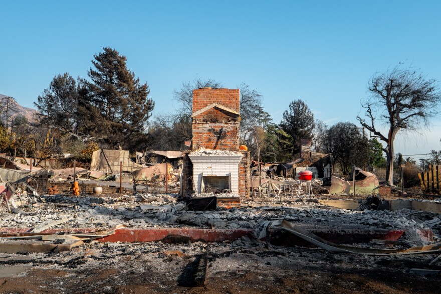 A brick chimney stands in the ruins of a home. A red grill is also visible.