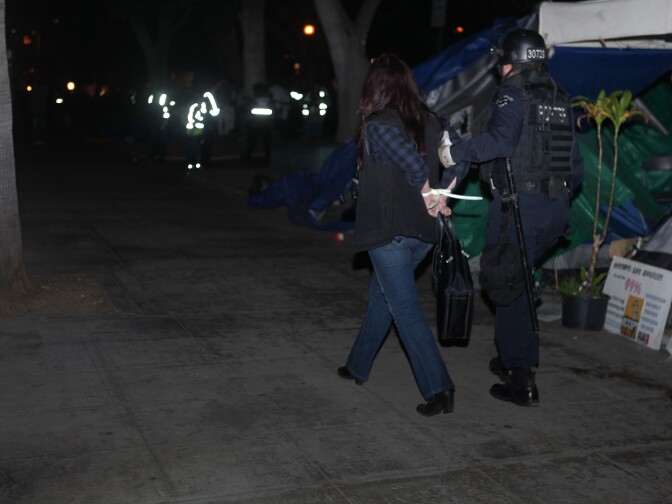An LAPD officer led an arrested protester to buses that were waiting to transfer detainees. Police arrested 292 protesters.