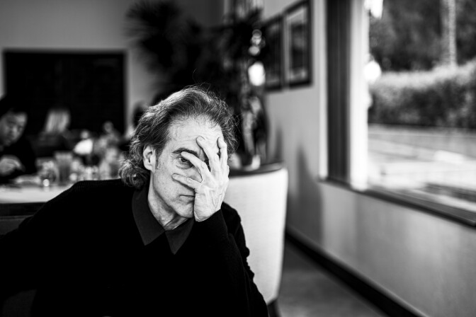 A photo of a man sitting at a dinner table, covering his face with one hand