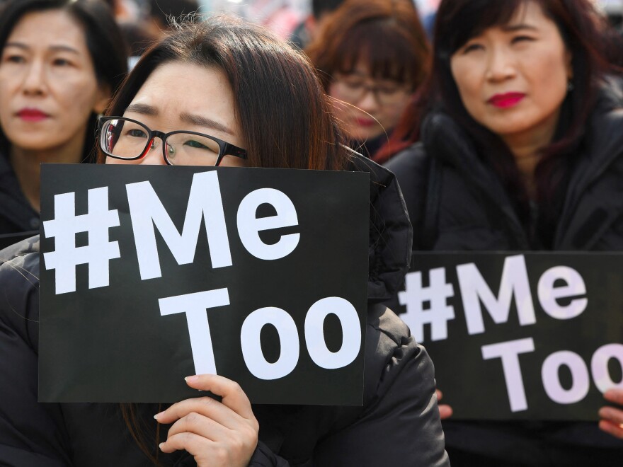 Women hold up black signs with white writing that reads: #Me Too