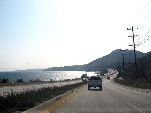 A highway with cars and the ocean on the left.
