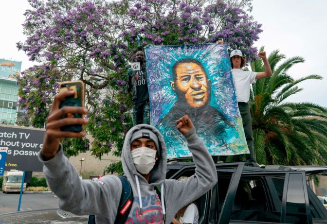 A protester poses next to a painting for George Floyd's family in Hollywood after curfew during a demonstration over the death of George Floyd while in Minneapolis Police custody, in Los Angeles, California, June 2, 2020. - Anti-racism protests have put several US cities under curfew to suppress rioting, following the death of George Floyd in police custody. (Photo by Kyle Grillot / AFP) (Photo by KYLE GRILLOT/AFP via Getty Images)