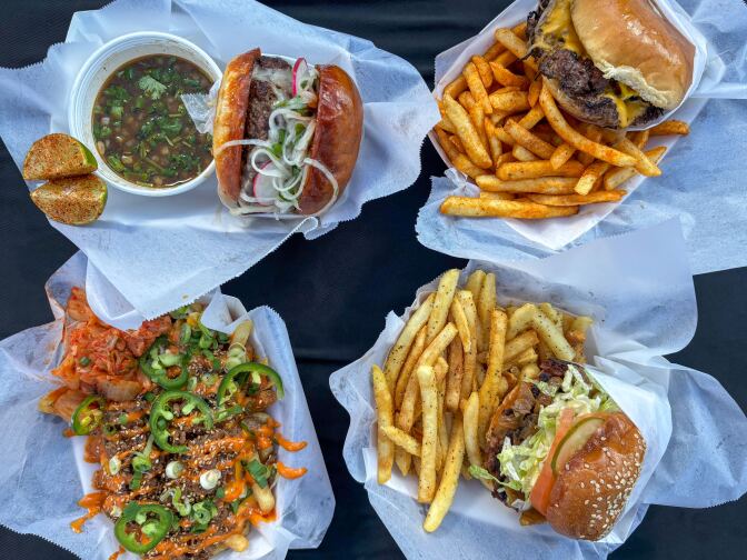 Four different plates of food, including three different types of burgers. The two on the right come with  fries and different seasonings. On the left is a burger next to a side of consomme, and a plate of dressed fries with an orange sauce and green sliced jalapenos. 