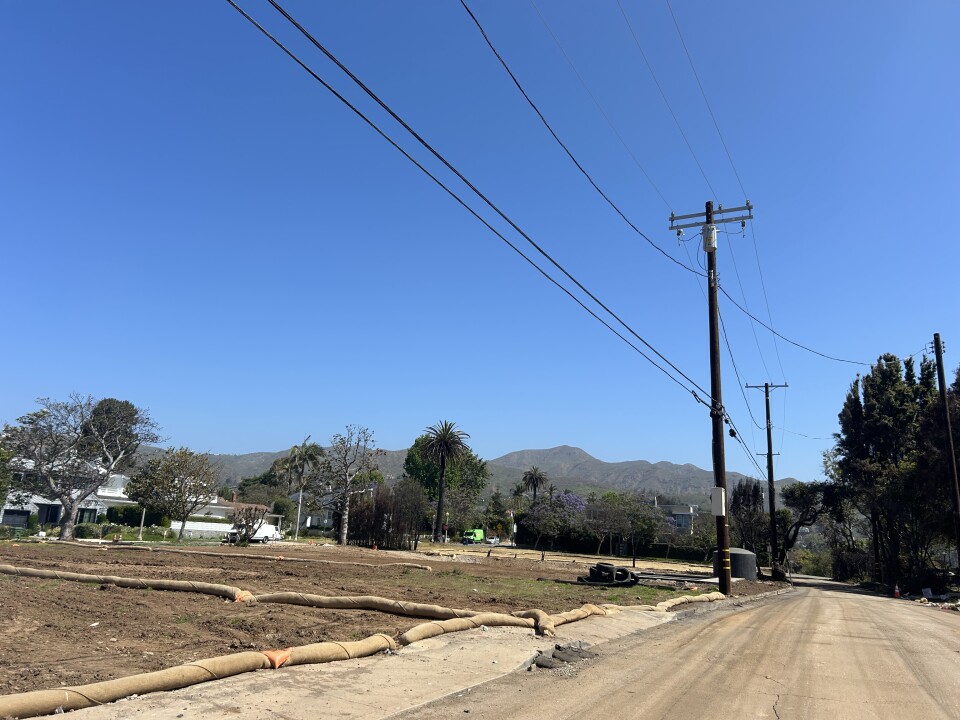 A street of empty dirt lots with mountains in the background and blue skies. 