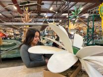 A girl with dark brown and medium-light skin tone holds a petal of a giant white flower.