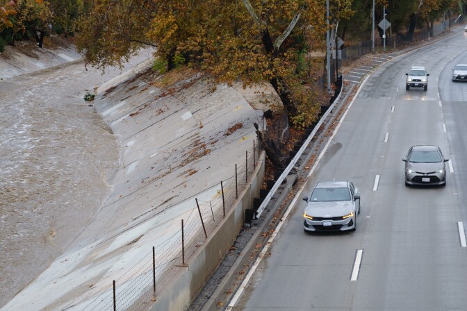 A rush of rain rolls down a pathway by a freeway with cars driving on it.