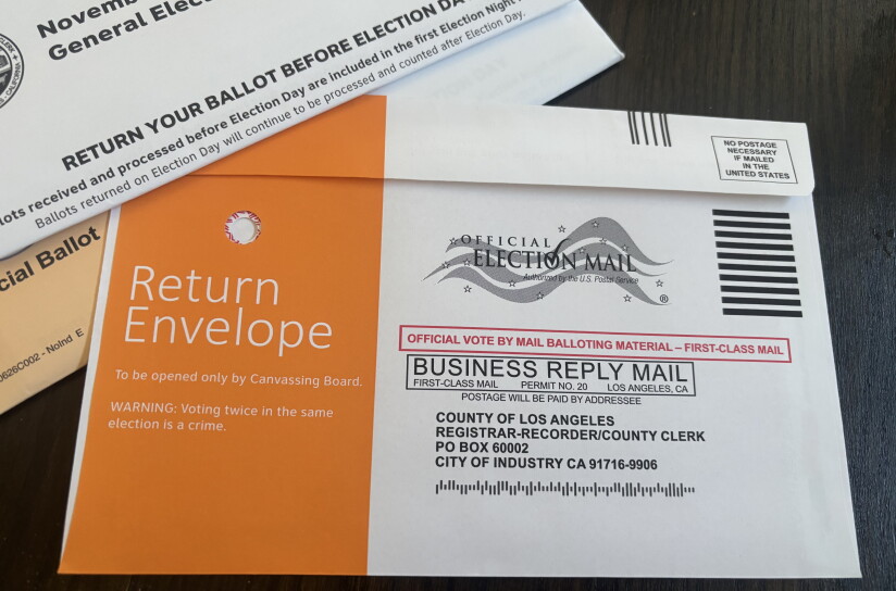 A white-and-orange ballot return envelope addressed to the LA County Registrar-Recorder, marked "Official Election Mail," with no postage required.