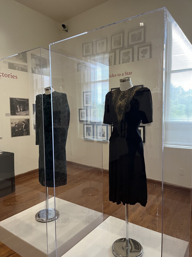 Two vintage dark dresses are on display behind acrylic boxes in a museum. 