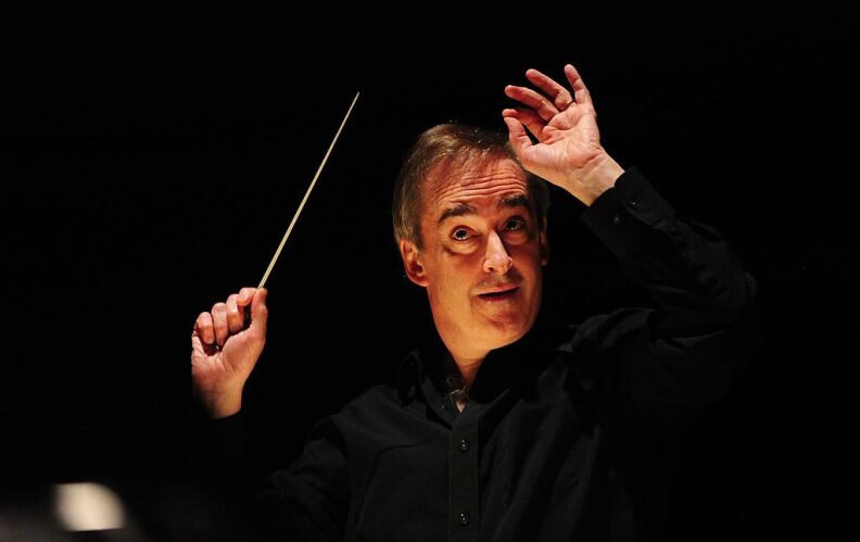 A male composer with his hands up in motion as he directs a rehearsal.