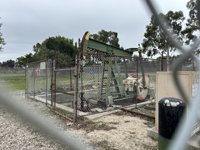 A green pumpjack surrounded by a chain link fence under cloudy skies. 