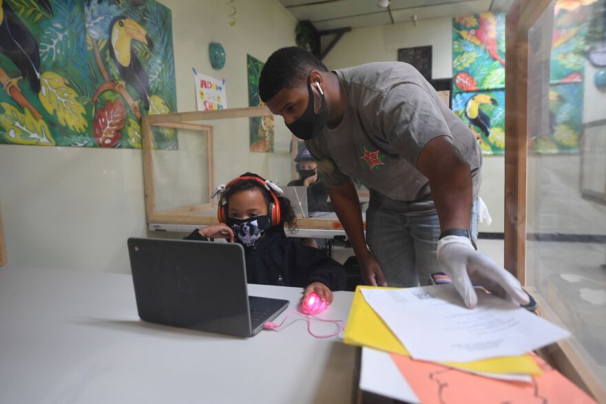 An instructor helps a student with her online school lesson at a desk separated from others by plastic barriers at STAR Eco Station Tutoring & Enrichment Center on September 10, 2020 in Culver City, California. - California public school students will continue to learn at home, in private learning pods, or at specialized enrichment centers like Star Eco Station as the coronavirus pandemic continues, after a lawsuit brought by the Orange County Board of Education seeking to compel the state to reopen public schools was shot down by the California Supreme Court on September 10. (Photo by Robyn Beck / AFP) (Photo by ROBYN BECK/AFP via Getty Images)