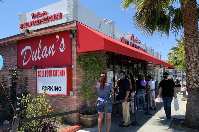 People wait outside a brick building with a red and white awning and a red sign with the restaurant's name