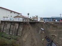 The collapse this week cut away part of a patio where several people can be seen standing. What looks like patio furniture and other construction materials have slid down the hillside along with the dirt. Another portion of the cliff is reinforced with wooden scaffolding. 