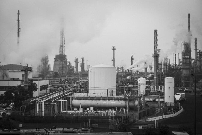A black and white photo shows the towers and tanks of an oil refinery.