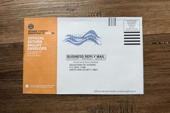 A close-up of a ballot return envelope from Orange County. The left side is orange and reads "Official Return Ballot Envelope."