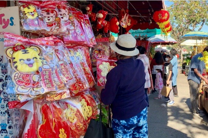 A woman in a hat, her back to the camera, browses Lunar New Year decorations on a busy street. 